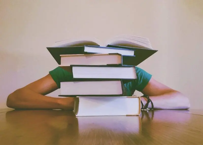 person's face blocked by stack of books