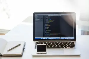 MacBook Pro with a mobile phone resting on the keyboard and a notebook